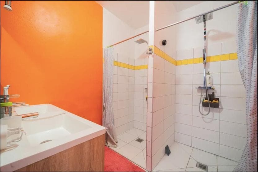 Salle de bain avec mur orange, double vasque et deux douches blanches à bande jaune.