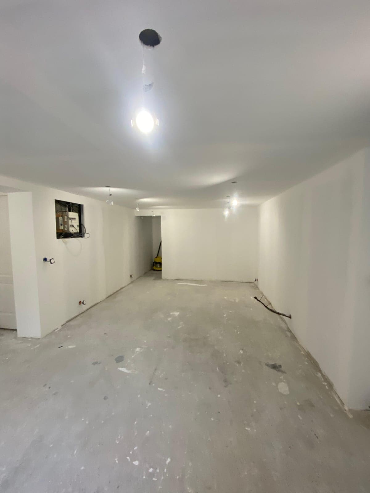 Pièce vide aux murs blancs et sol en béton brut en cours de rénovation intérieure.